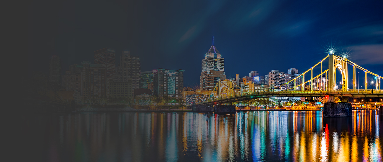 A brightly lit bridge and cityscape at night, reflecting on the water.