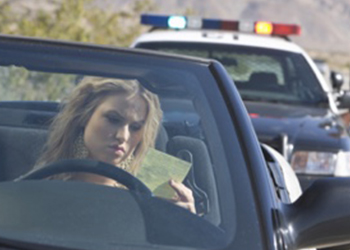 a-woman-in-a-convertible-receiving-a-ticket-from-a-police-car-behind-her.jpg